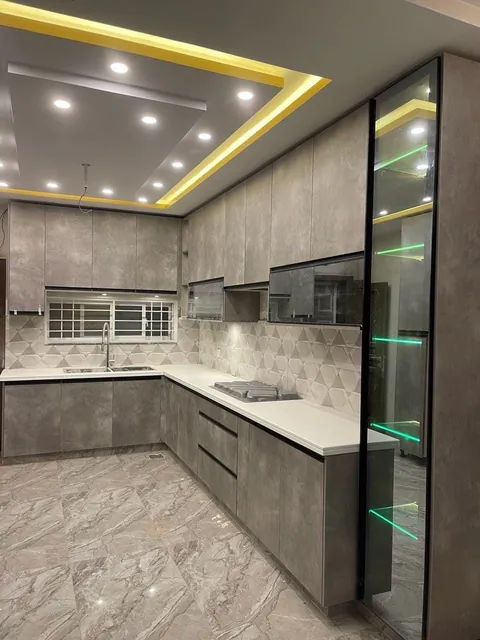 Grey concrete-look kitchen with a glass tall unit and cove lit ceiling